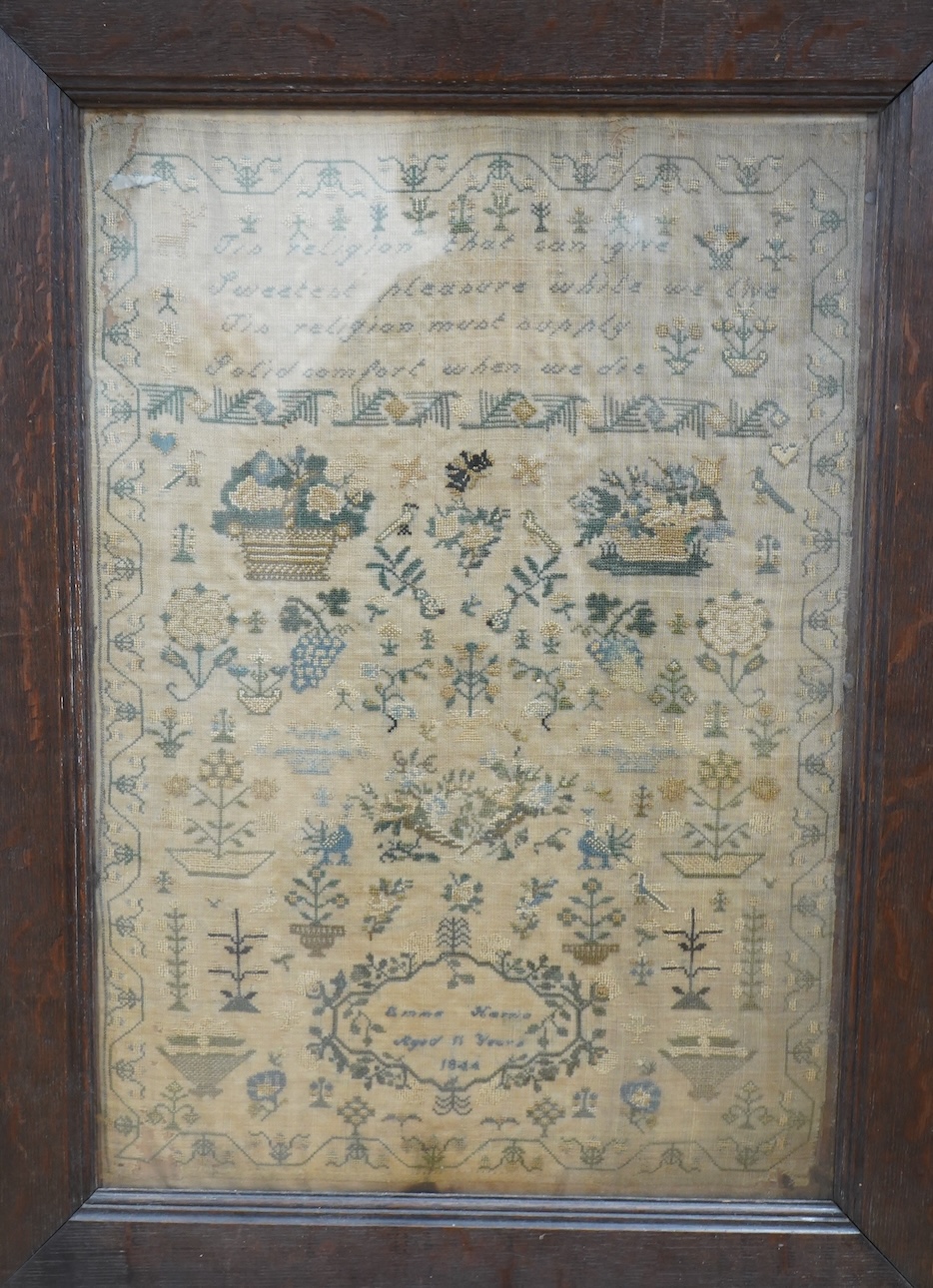 A framed 19th century sampler by Emma Harris, aged 11years, dated 1844. Worked with a verse and large baskets of flowers, with many spot motifs of flowers and birds amongst stylistic trees, worked within a vining border,